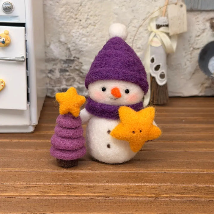 Front view of Starlight Snowman felt figurine with a purple winter hat, matching scarf, orange carrot nose, and yellow star beside a purple felt Christmas tree.