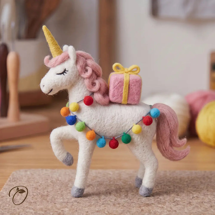 Left-facing felt unicorn with a curled pink mane, closed eyes, one front leg raised and a pink present on its back.