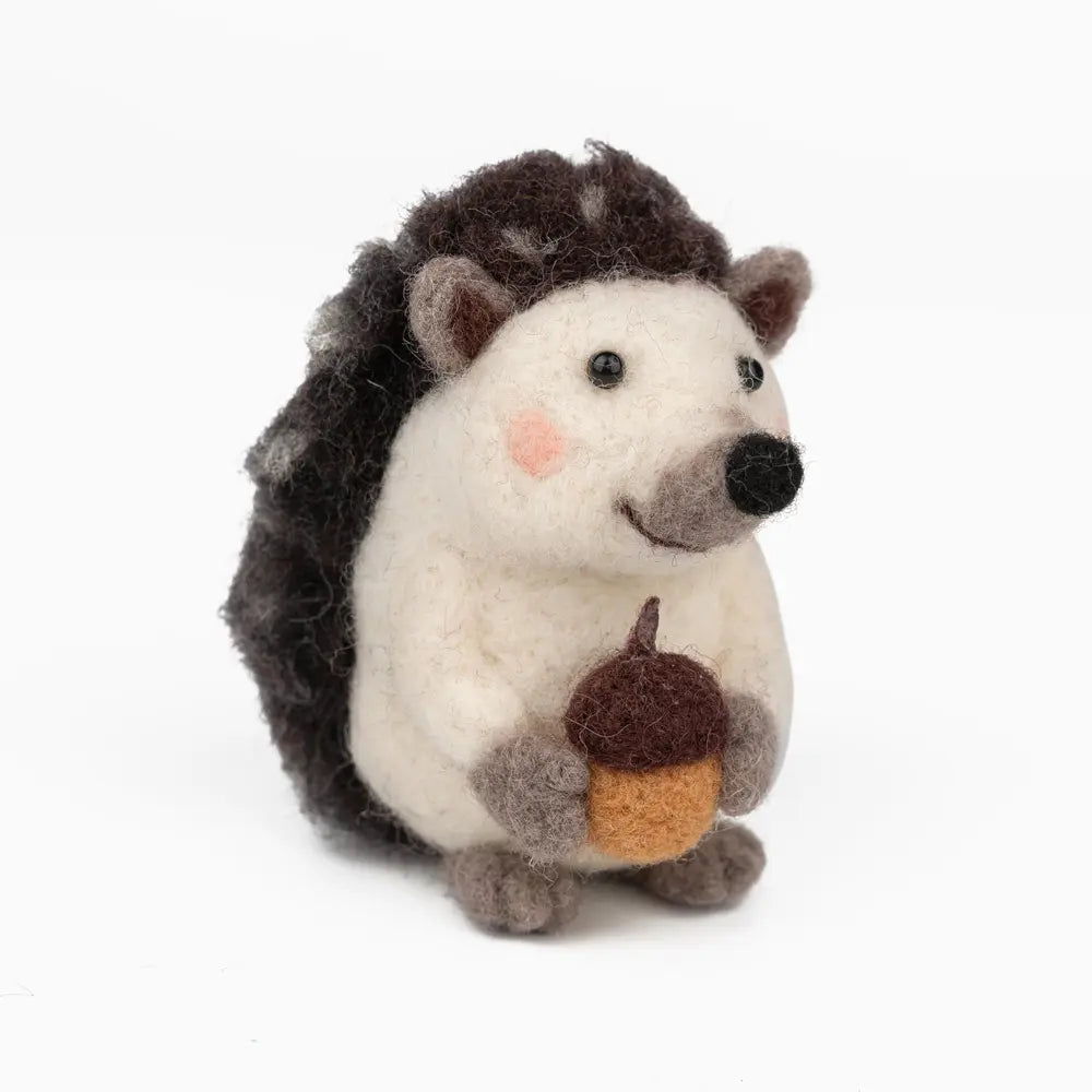 Stuffed hedgehog toy holding an acorn on a white background