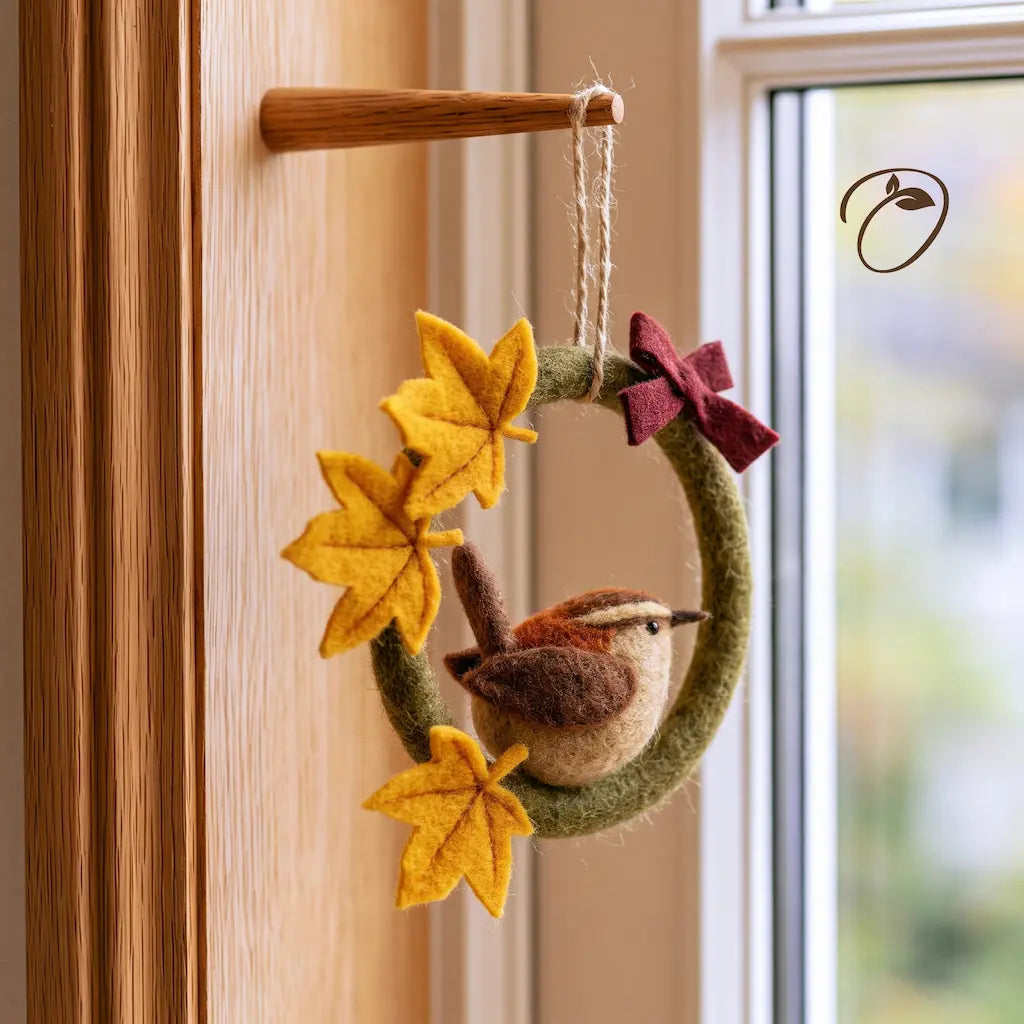 Angled view of a felt songbird wreath showing the sculpted brown bird, layered golden maple leaves, and burgundy bow.