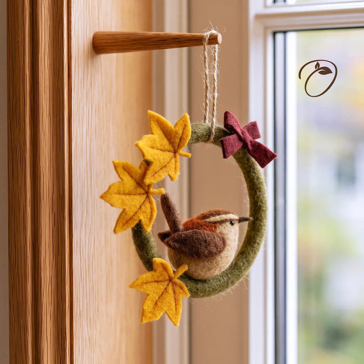 Angled view of a felt songbird wreath showing the sculpted brown bird, layered golden maple leaves, and burgundy bow.
