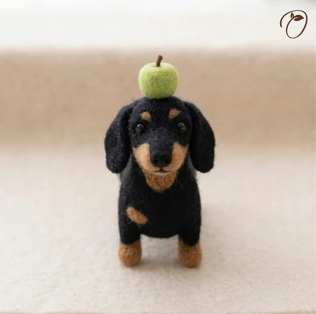 Felted dachshund toy with a green apple on its head against a beige background
