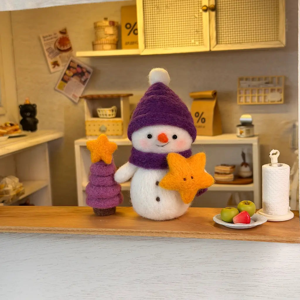 Handmade Starlight Snowman felt figurine holding a yellow star beside a miniature purple Christmas tree in a cozy dollhouse kitchen scene.