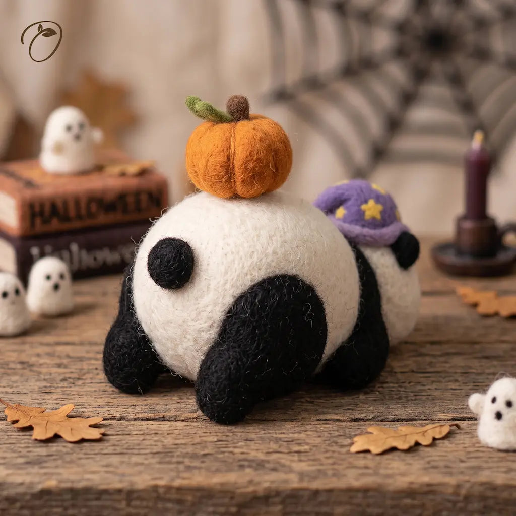 Rear view of a felt panda figurine showing its round body, black tail and orange pumpkin with a green leaf