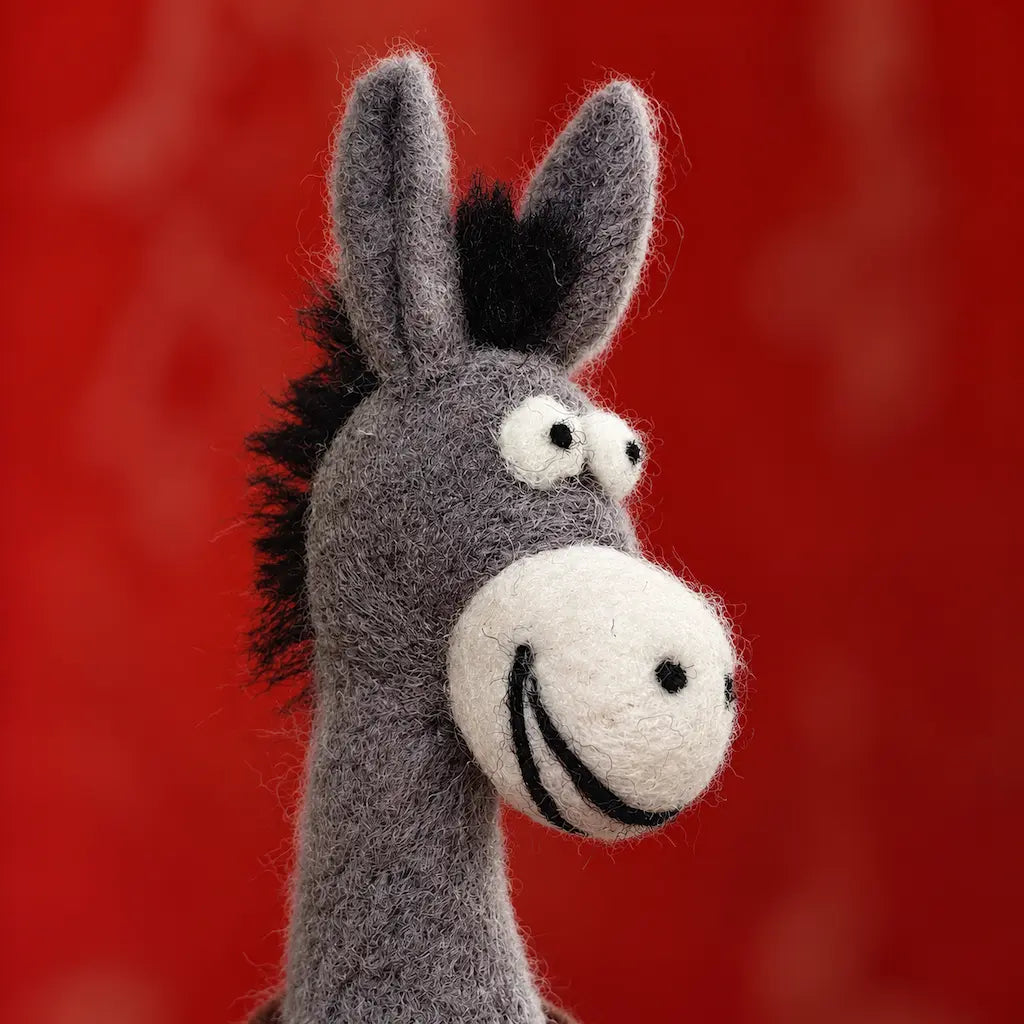 Close-up of a gray felt donkey’s smiling cream muzzle, wide eyes, tall ears, and textured black mane.