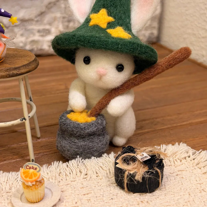 Handmade Starlit Cauldron Bunny wool felt figurine wearing a green starry wizard hat, sitting beside a gray cauldron with yellow potion and a brown stirring stick.
