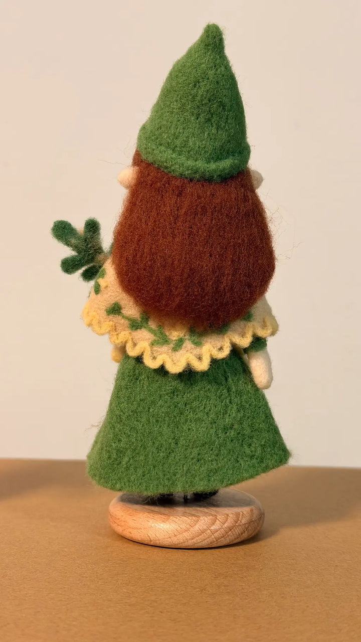 Handmade gnome figurine with green hat and dress on a wooden base against a beige background