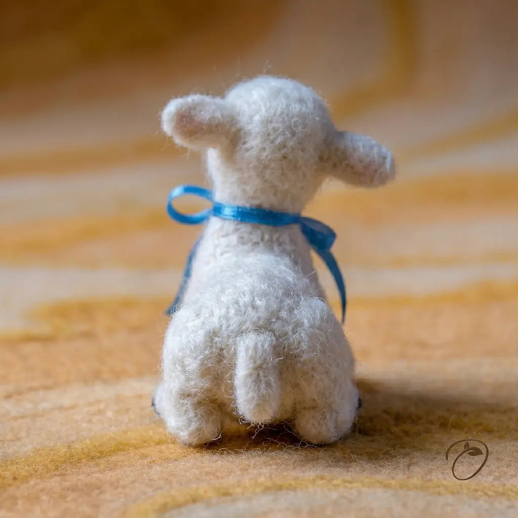 Small white stuffed animal with a blue ribbon on a textured orange surface