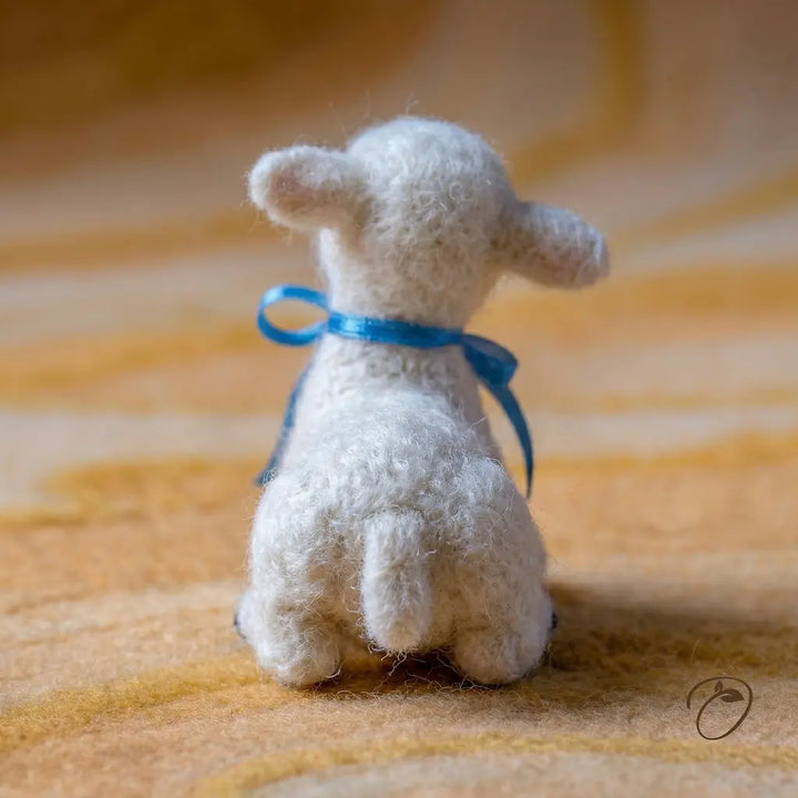 Small white stuffed animal with a blue ribbon on a textured orange surface