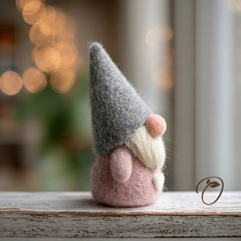 Felted gnome figurine with a gray hat and pink body on a wooden surface with a blurred background