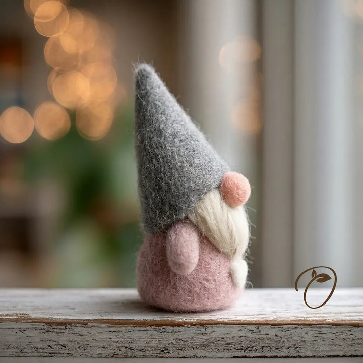 Felted gnome figurine with a gray hat and pink body on a wooden surface with a blurred background