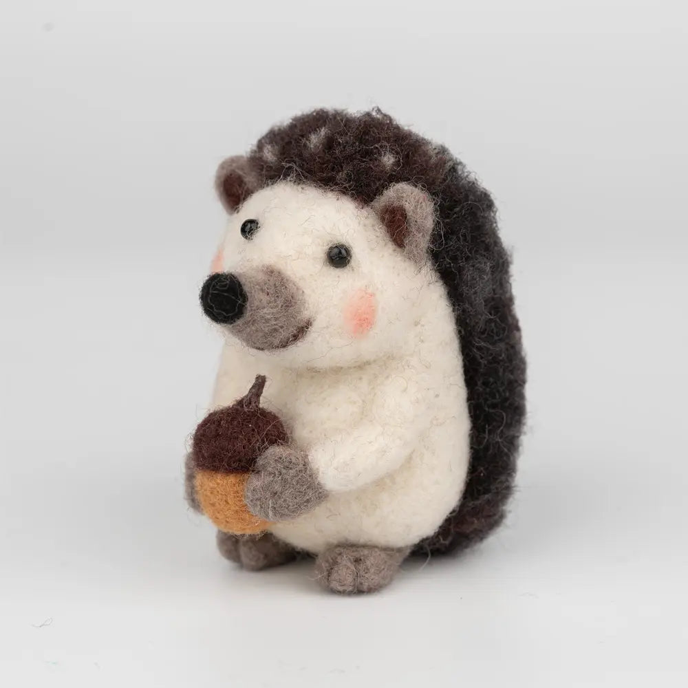 Stuffed hedgehog toy holding an acorn on a white background