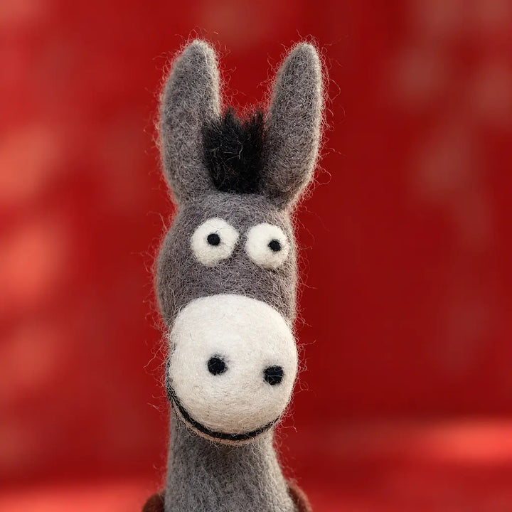 Front close-up of a smiling wool felt donkey with tall gray ears, white eyes, black nostrils, and a cream muzzle.