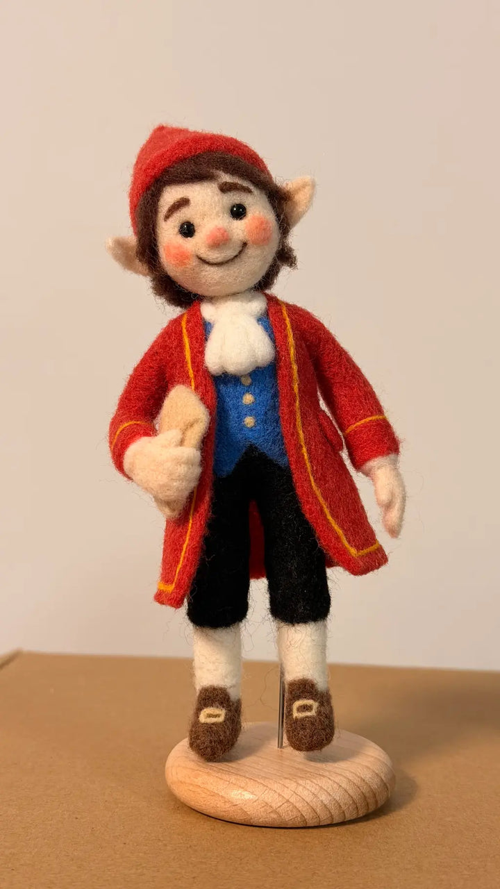 Felted elf figurine wearing a red coat and hat on a wooden base against a plain background