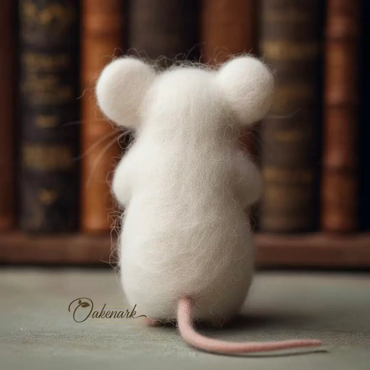 White felted mouse toy with a pink tail on a surface with books in the background
