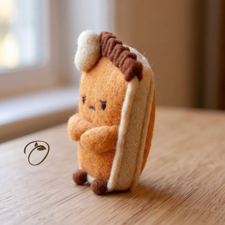 Side view of a grumpy pumpkin pie felt figurine showing its folded arms, cream-colored edging, brown crust, and small feet.