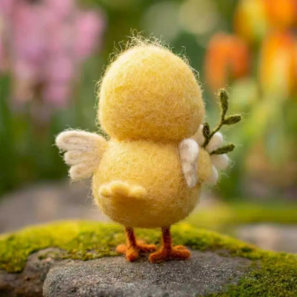 Yellow felted chick figurine with flowers on a stone surface with a blurred floral background