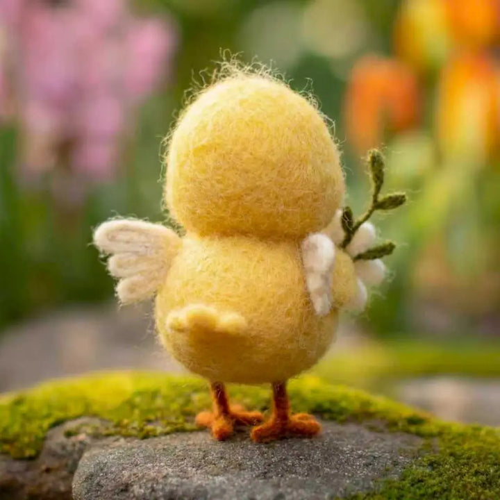 Yellow felted chick figurine with flowers on a stone surface with a blurred floral background