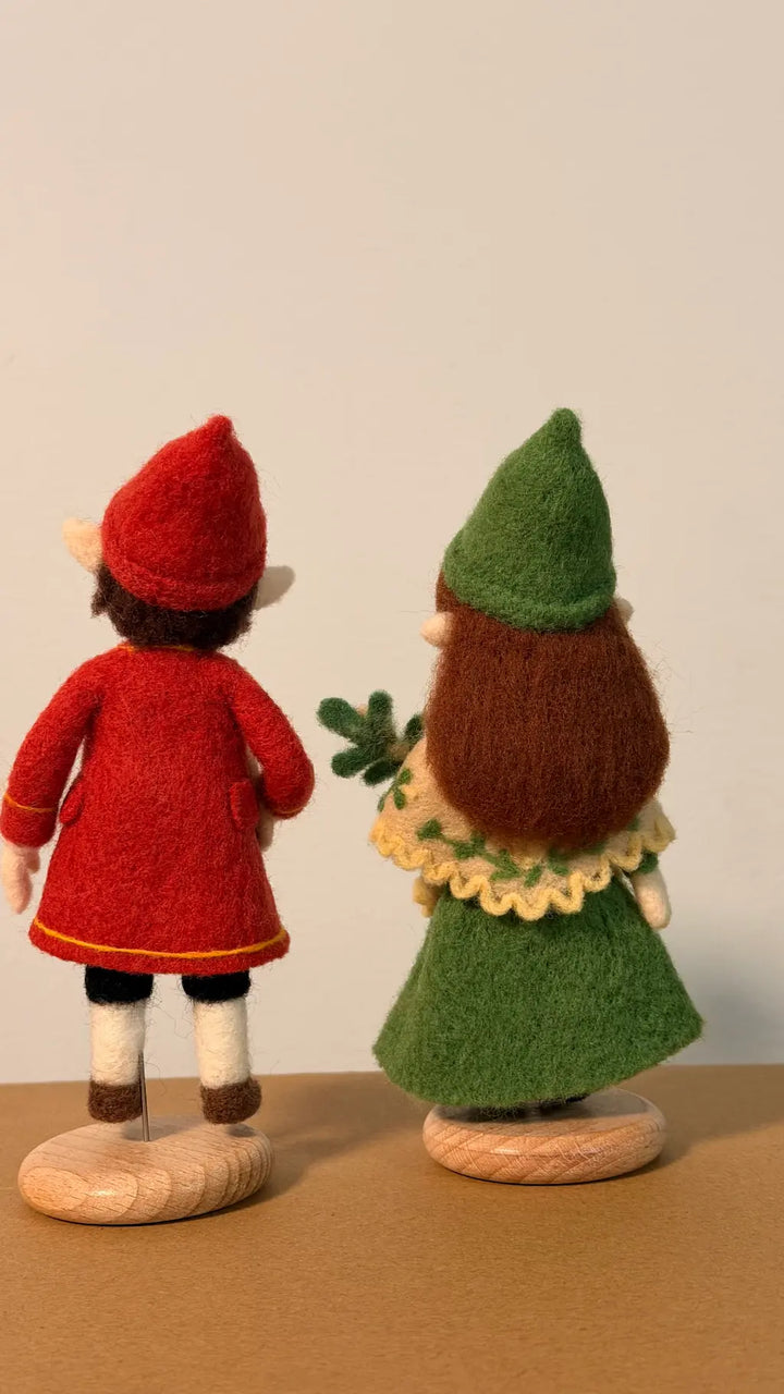 Two felted dolls, one in a red outfit and the other in a green outfit, standing on a neutral background.