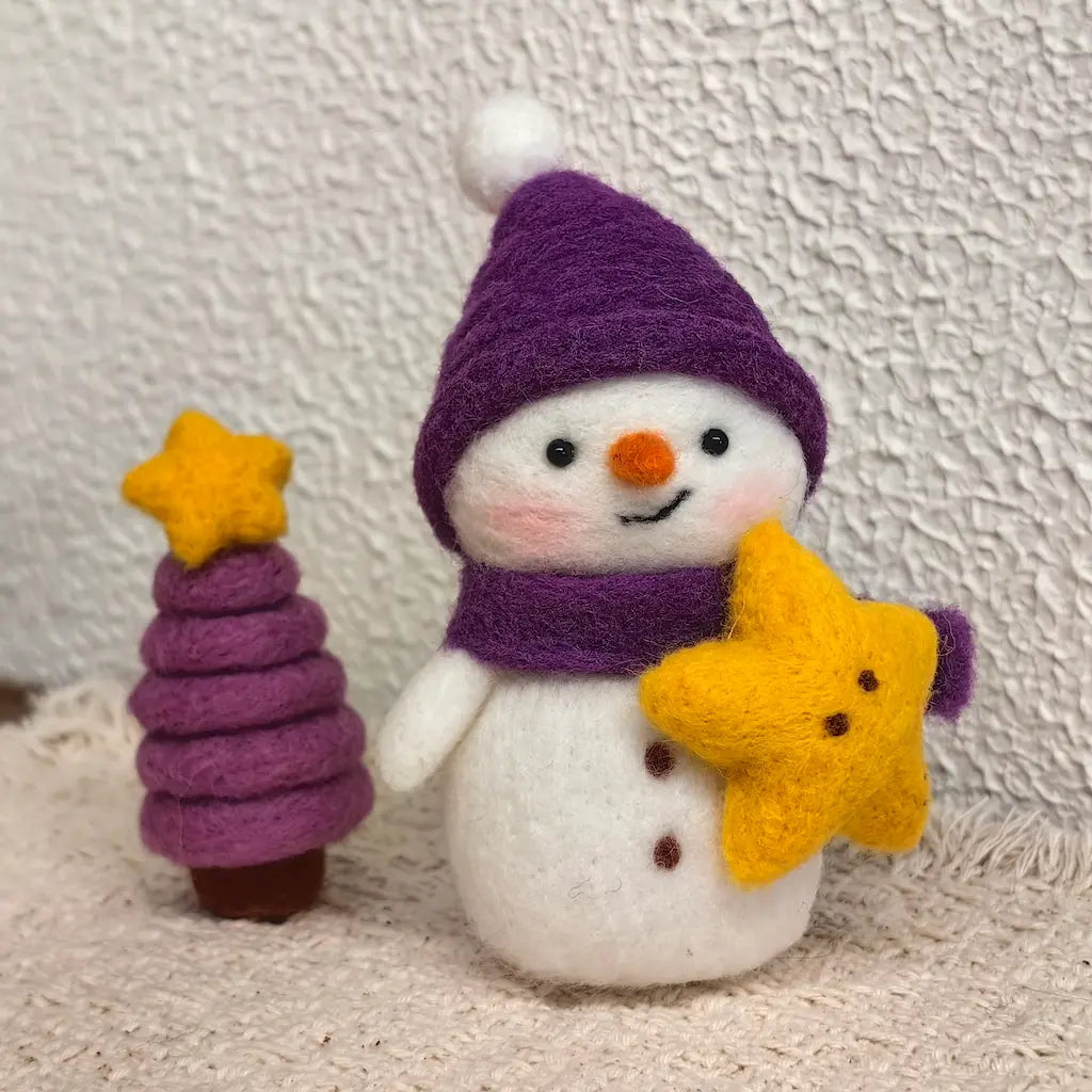 Handmade Starlight Snowman wool felt figurine wearing a purple winter hat and scarf, holding a yellow star beside a miniature purple Christmas tree topped with a golden star.