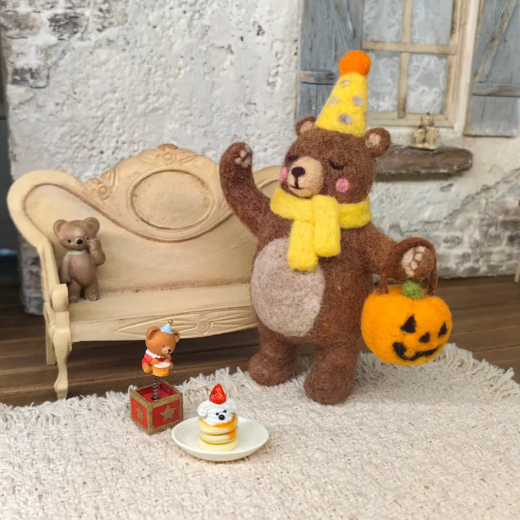 Party Bear felt figurine holding a jack-o-lantern basket with miniature birthday cake in a cozy celebration scene