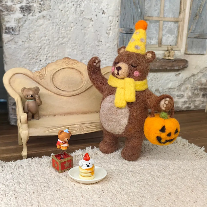 Party Bear felt figurine holding a jack-o-lantern basket with miniature birthday cake in a cozy celebration scene