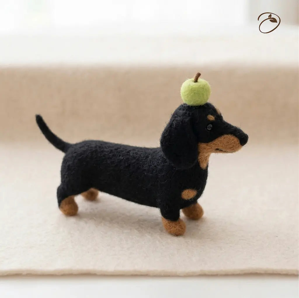 Felted dachshund toy with a green apple on its head against a beige background