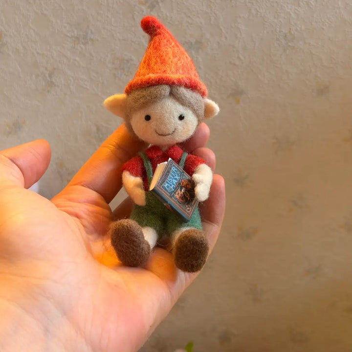 Small plush toy with a red hat and overalls held in a hand against a neutral background