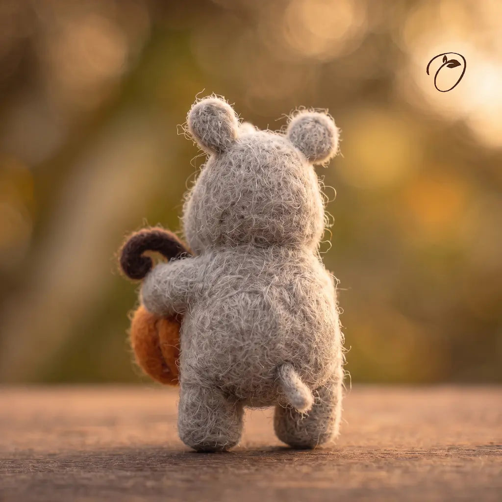 Back view of a gray wool felt rhino with rounded ears and a short tail, with part of its orange pumpkin visible at the side.