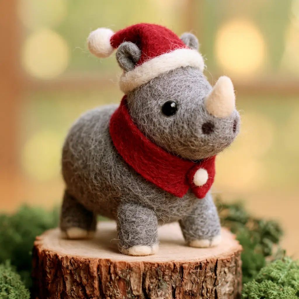 Front three-quarter view of a gray felt rhino wearing a red Santa hat and scarf, standing on a wood slice.