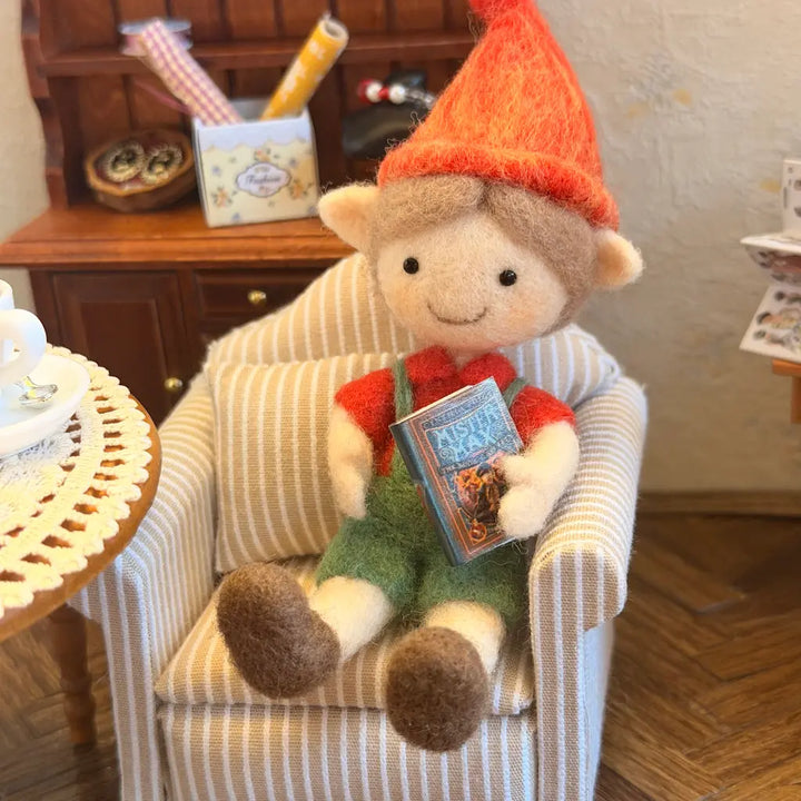 Stuffed elf sitting in a chair holding a book in a cozy room.