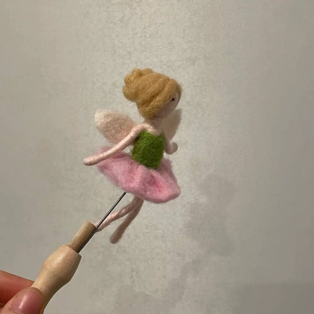 Felted fairy held by a needle against a plain background