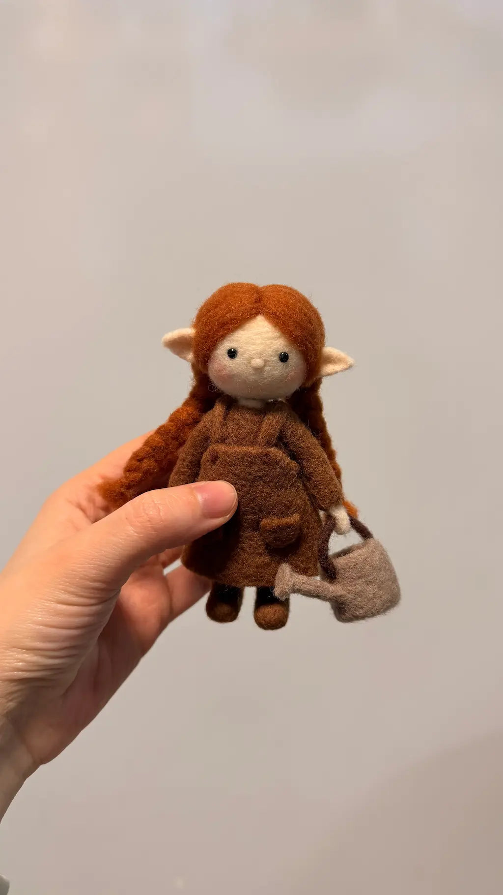 Hand holding a small brown plush toy with red hair against a plain background