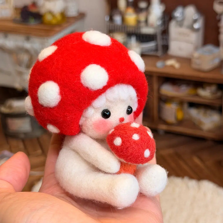 A small white felt doll with a large red mushroom cap and holding a smaller red mushroom, being held in a person&