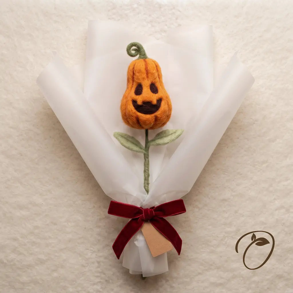 Elongated orange wool felt pumpkin with a playful face and curled green stalk, wrapped as a bouquet