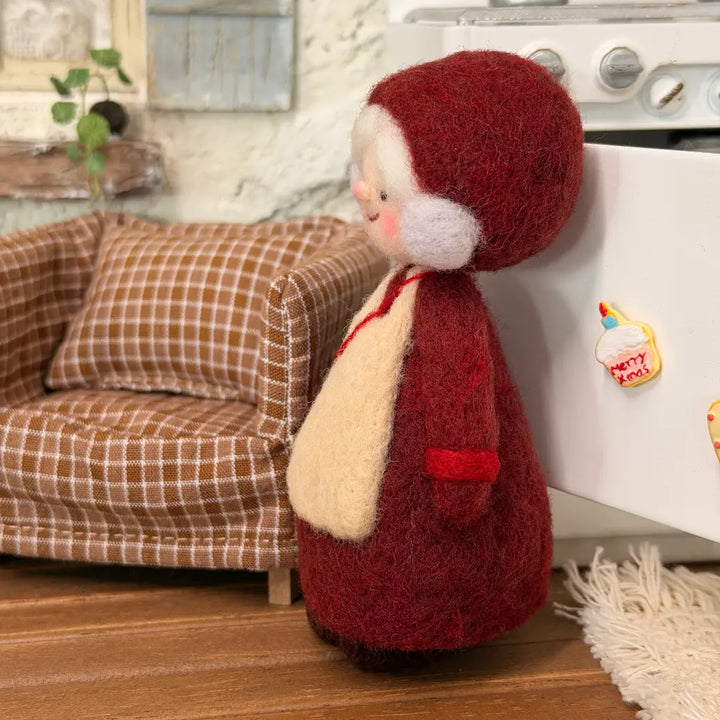 Side view of Burgundy Bonnet Mrs. Claus felt figurine showing her rounded bonnet, fluffy white hair, burgundy outfit, and small red bag.