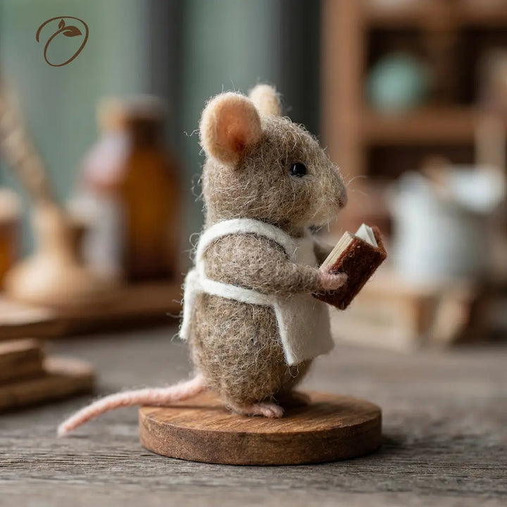 Felted mouse figurine holding a book on a wooden base with a blurred background