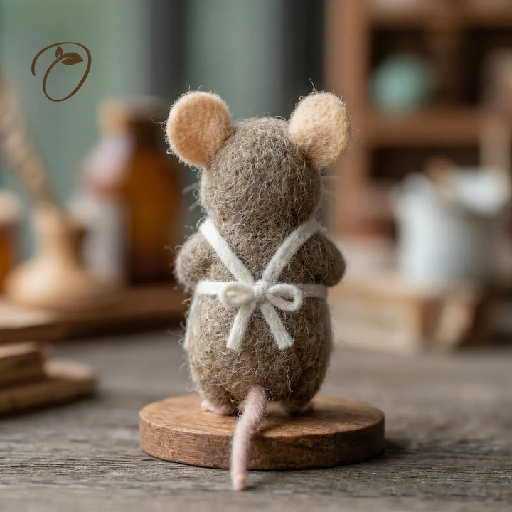 Felted mouse figurine with a white bow on a wooden base in a warm-toned room.
