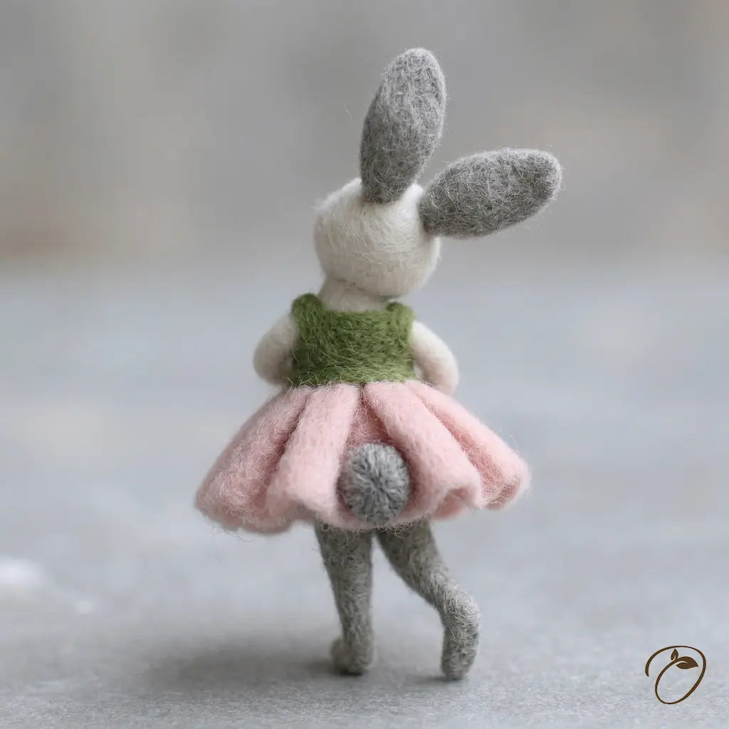 Toy rabbit with a green sweater and pink skirt on a neutral background