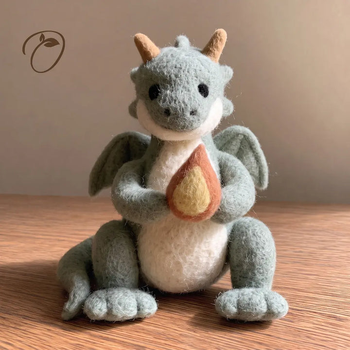 Front view of a sage green felt dragon with tan horns, two wings and an orange felt flame with a yellow center.