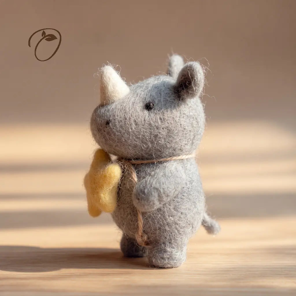Side view of a gray felt rhino with an ivory-colored horn, a yellow star at its chest and a small curled tail.