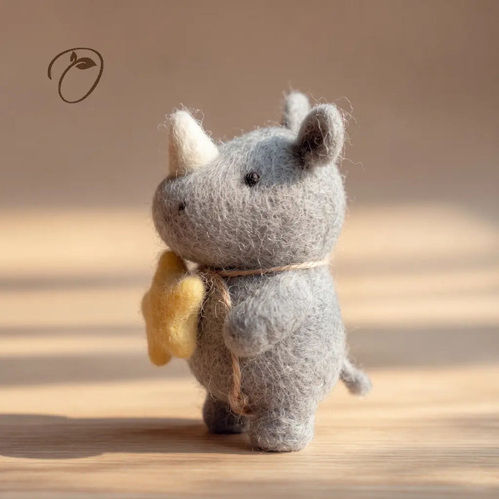 Side view of a gray felt rhino with an ivory-colored horn, a yellow star at its chest and a small curled tail.