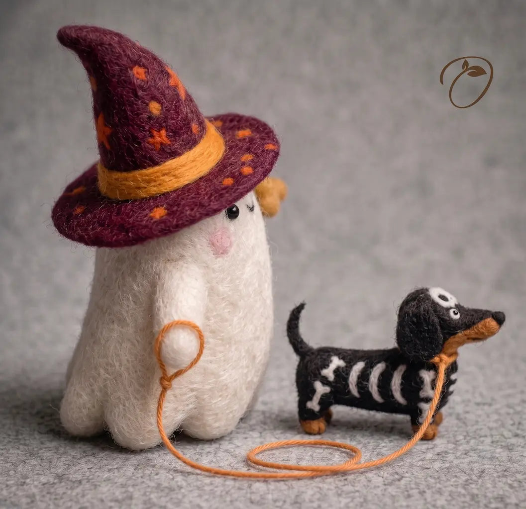 A handcrafted felt art piece featuring a white ghost wearing a purple witch hat with orange stars and a yellow band, holding an orange leash attached to a black and white dachshund with skeleton details, set against a textured gray background.