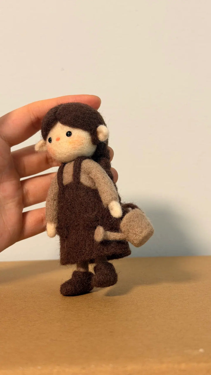 Small felt doll with brown hair, dress, and shoes held by a hand against a plain background