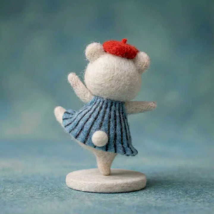 Felted animal figurine, possibly a cat, wearing a red hat and blue dress on a teal background