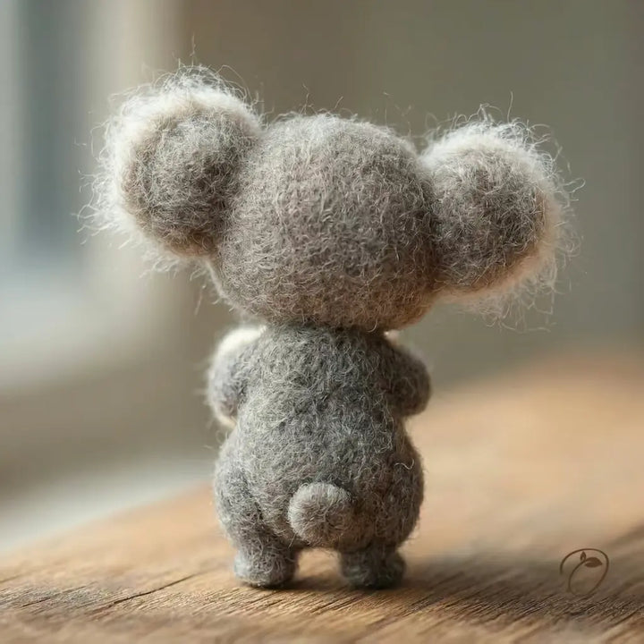 Small gray plush toy resembling a koala on a wooden surface with a blurred background