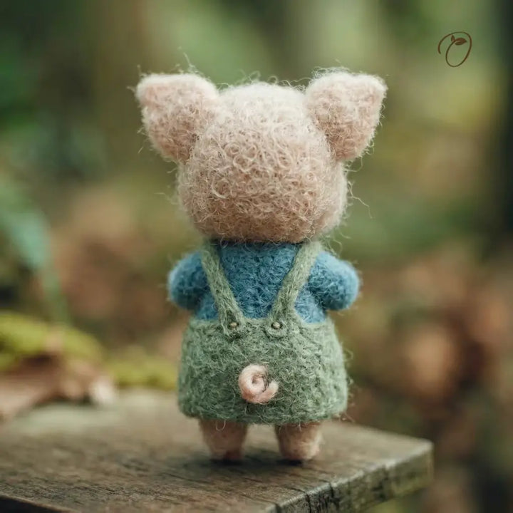 Small plush toy with a fluffy pink head and green overalls standing on a wooden surface with a blurred natural background.