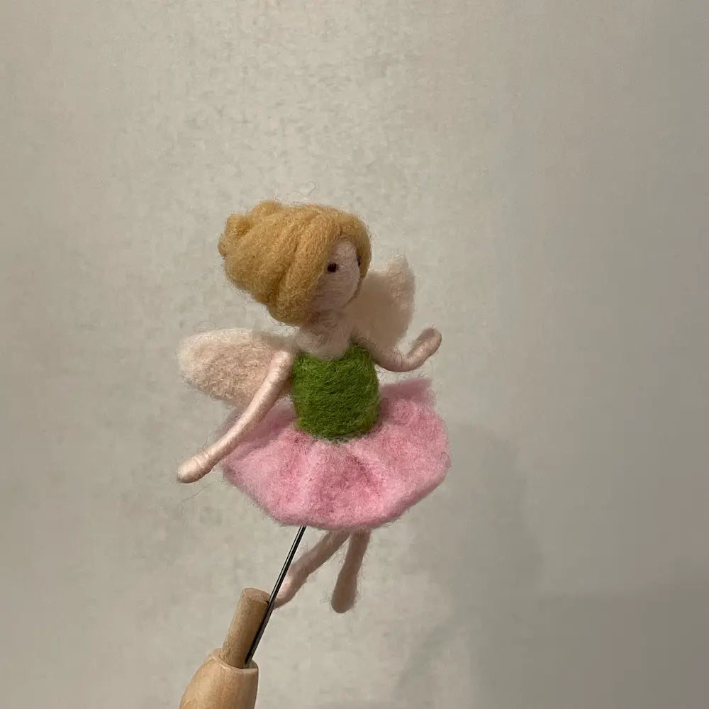Felted fairy figurine on a stick against a plain background
