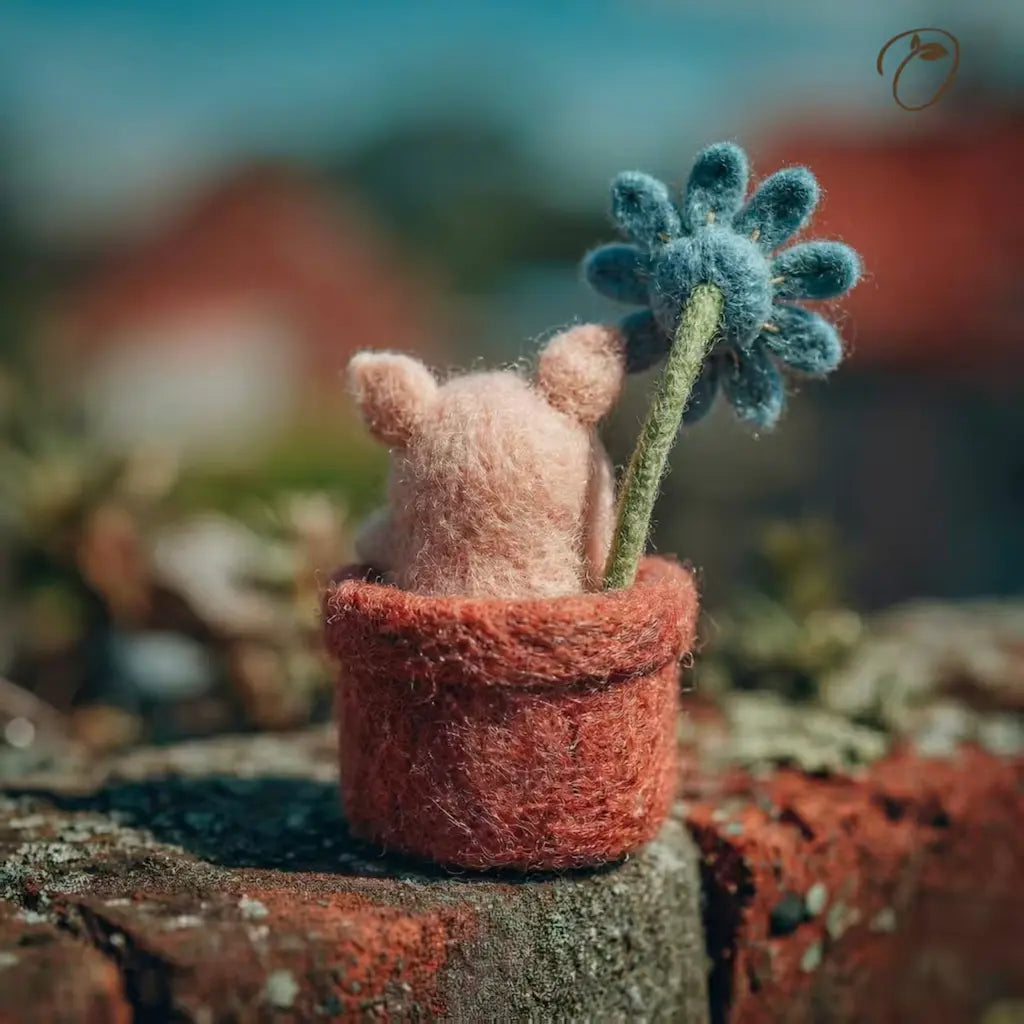 Small pink creature with a blue flower in a textured pot on a blurred natural background