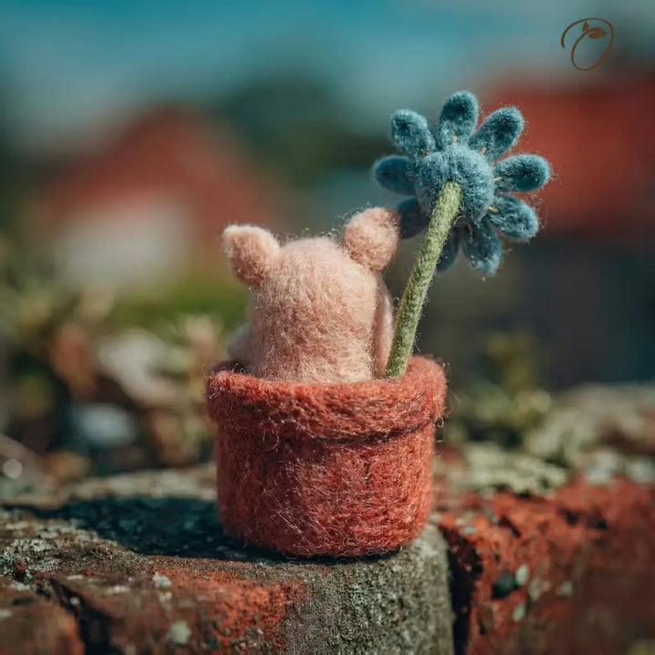 Small pink creature with a blue flower in a textured pot on a blurred natural background